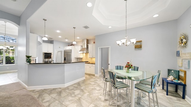 kitchen with decorative backsplash, appliances with stainless steel finishes, wall chimney exhaust hood, decorative light fixtures, and white cabinetry