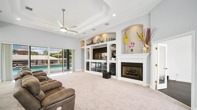 carpeted living room with built in shelves, a towering ceiling, a tray ceiling, and ceiling fan