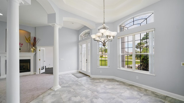 unfurnished dining area with ornate columns, light colored carpet, a healthy amount of sunlight, and a notable chandelier