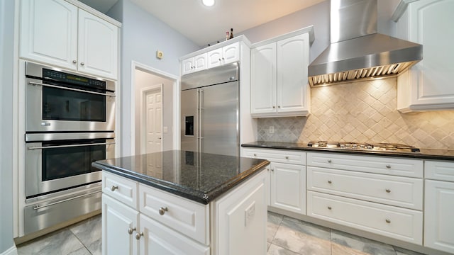 kitchen featuring a center island, wall chimney exhaust hood, dark stone countertops, white cabinets, and appliances with stainless steel finishes