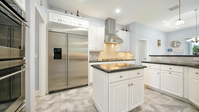 kitchen featuring appliances with stainless steel finishes, backsplash, wall chimney range hood, white cabinets, and hanging light fixtures