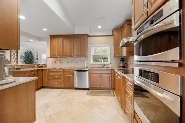 kitchen with tasteful backsplash, appliances with stainless steel finishes, light stone countertops, and sink