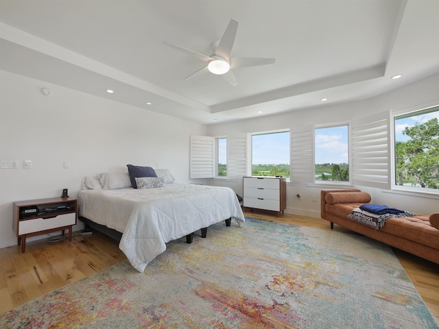 bedroom featuring light hardwood / wood-style flooring, a raised ceiling, and ceiling fan