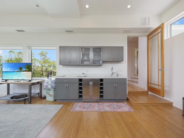 bar with gray cabinets, high end fridge, light hardwood / wood-style floors, and sink