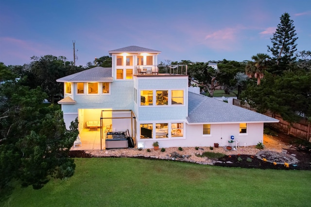 back house at dusk featuring a lawn, a balcony, and a patio