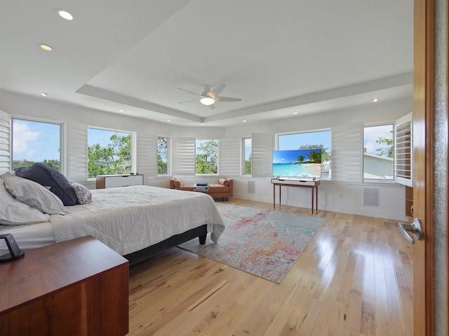 bedroom featuring multiple windows, a tray ceiling, light hardwood / wood-style flooring, and ceiling fan