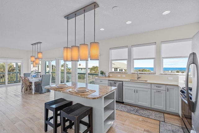 kitchen with a kitchen island, sink, hanging light fixtures, stainless steel appliances, and a water view