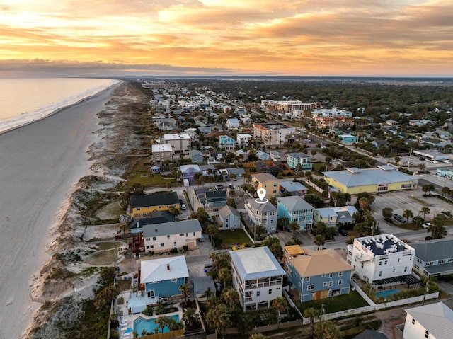 aerial view at dusk featuring a water view and a beach view