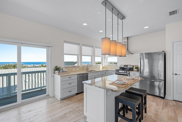 kitchen featuring a breakfast bar area, appliances with stainless steel finishes, a center island, a water view, and decorative light fixtures