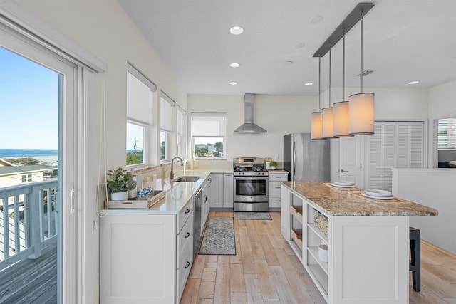 kitchen with wall chimney exhaust hood, sink, white cabinetry, hanging light fixtures, and appliances with stainless steel finishes