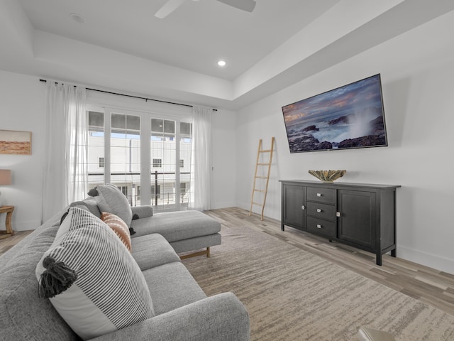 living room with ceiling fan, light hardwood / wood-style flooring, and a raised ceiling