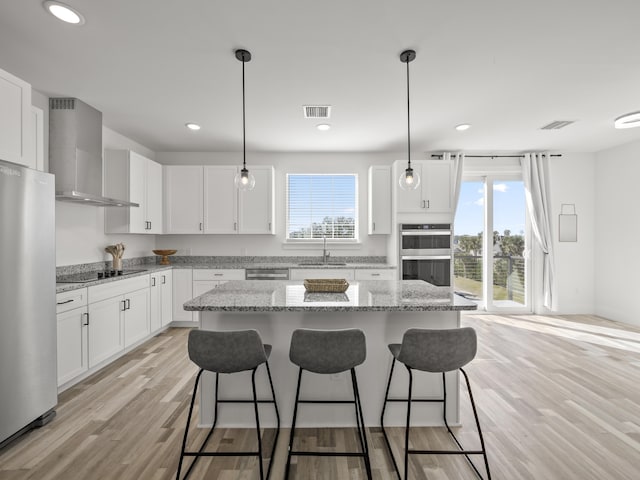 kitchen featuring white cabinets, stainless steel appliances, wall chimney range hood, and a center island