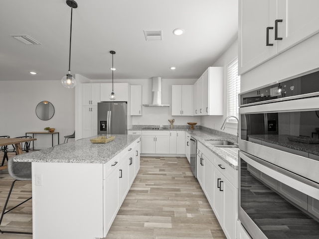 kitchen with wall chimney exhaust hood, stainless steel appliances, a kitchen island, white cabinets, and sink