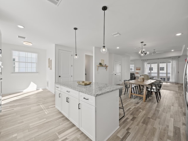 kitchen with decorative light fixtures, white cabinetry, a center island, light stone counters, and light hardwood / wood-style floors