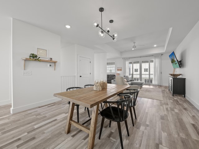 dining area featuring ceiling fan with notable chandelier, a tray ceiling, and light hardwood / wood-style flooring