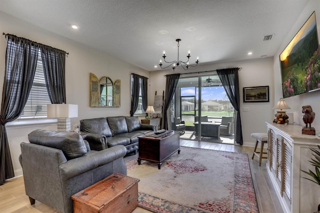 living room featuring baseboards, visible vents, an inviting chandelier, a textured ceiling, and light wood-type flooring