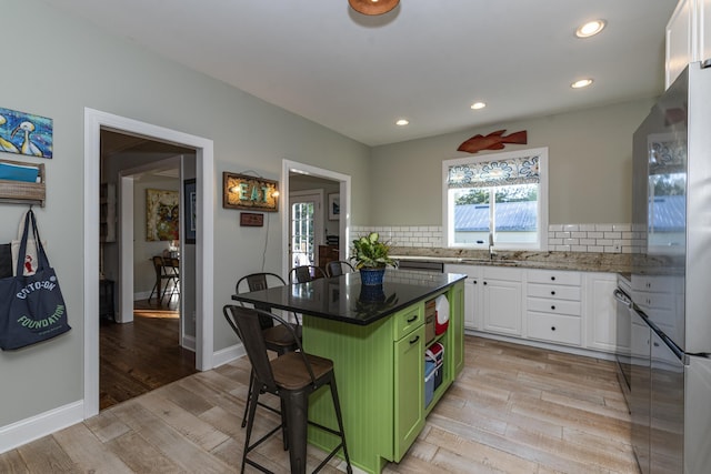 kitchen with a kitchen island, a breakfast bar, white cabinetry, backsplash, and green cabinetry