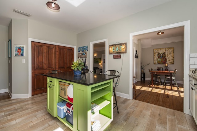 kitchen with a breakfast bar area, green cabinets, a kitchen island, and light wood-type flooring