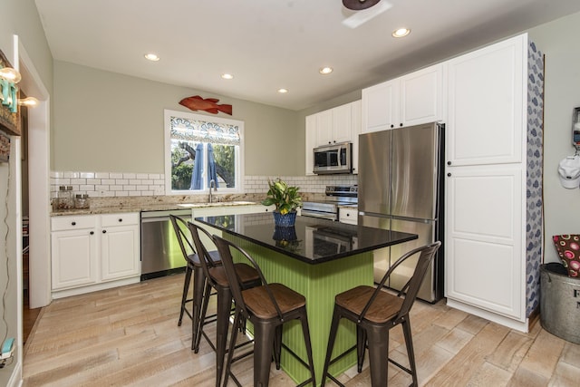 kitchen featuring dark stone countertops, stainless steel appliances, light wood-type flooring, and white cabinets