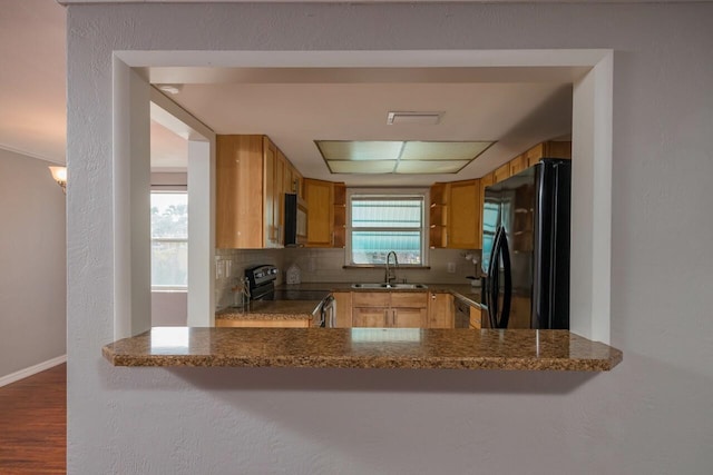 kitchen featuring sink, dark stone countertops, tasteful backsplash, black appliances, and kitchen peninsula