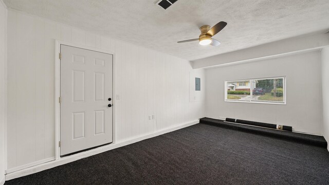 carpeted empty room featuring electric panel, ceiling fan, wooden walls, and a textured ceiling