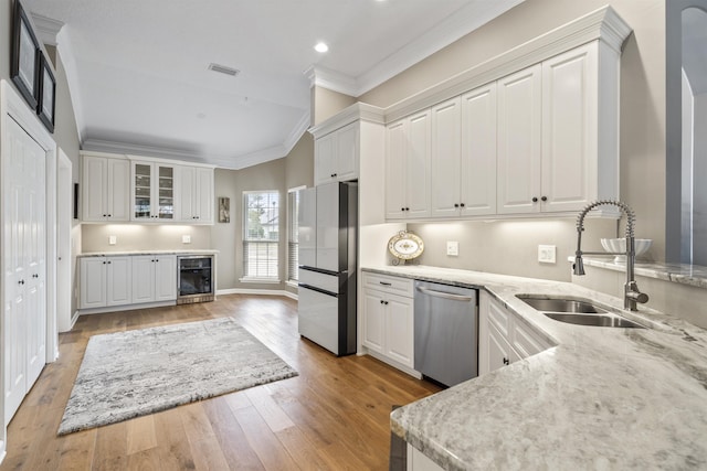 kitchen with light wood finished floors, beverage cooler, ornamental molding, stainless steel appliances, and a sink