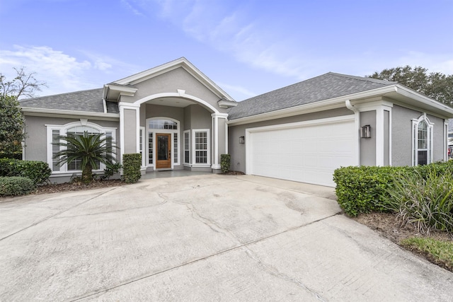 ranch-style house featuring a shingled roof, concrete driveway, a garage, and stucco siding