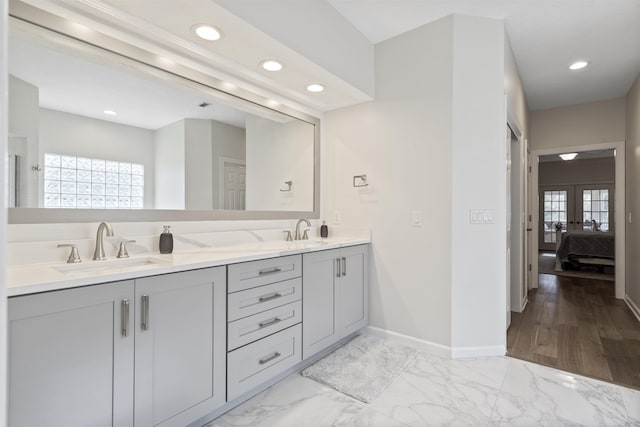 ensuite bathroom featuring marble finish floor, a sink, and baseboards