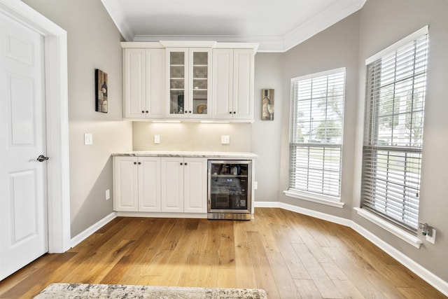 bar with light wood finished floors, ornamental molding, a bar, beverage cooler, and baseboards