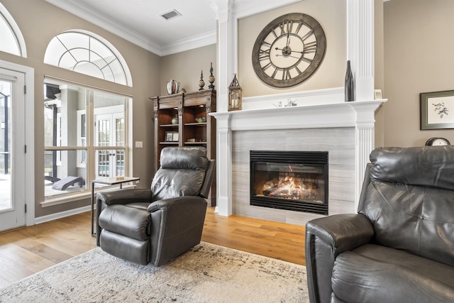 living area with ornamental molding, a tiled fireplace, wood finished floors, and visible vents