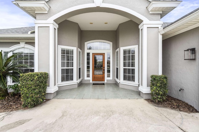 property entrance with roof with shingles and stucco siding