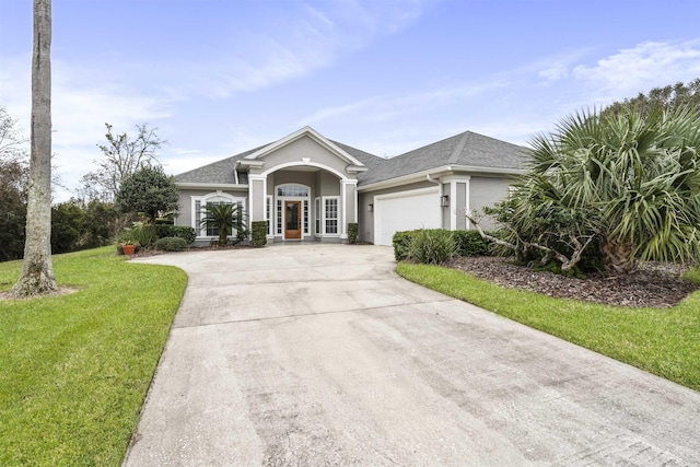 view of front of property with a garage, driveway, a shingled roof, stucco siding, and a front yard