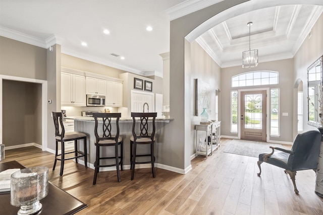 entrance foyer with arched walkways, baseboards, crown molding, and light wood finished floors