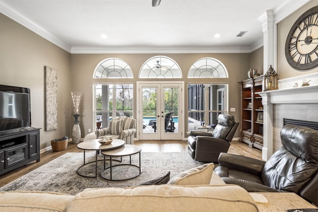 living area with baseboards, a tile fireplace, ornamental molding, wood finished floors, and french doors