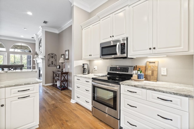 kitchen with crown molding, light wood finished floors, stainless steel appliances, visible vents, and white cabinets