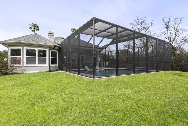 rear view of house with a lanai, a yard, roof with shingles, an outdoor pool, and a chimney