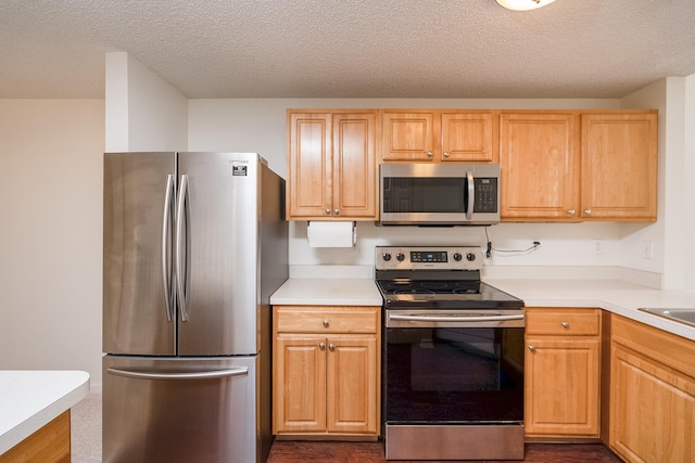 kitchen featuring stainless steel appliances, light brown cabinets, and a textured ceiling