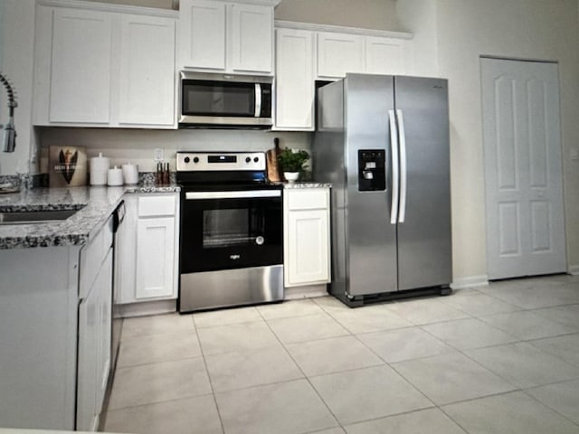 kitchen featuring sink, appliances with stainless steel finishes, white cabinetry, light stone counters, and light tile patterned flooring