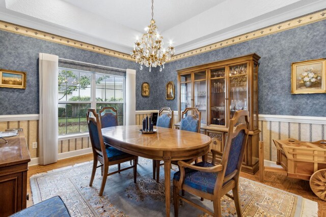 613 Wild Bird Ln, Saint Augustine, FL 32080 - dining room with wallpapered walls, a chandelier, a wainscoted wall, wood finished floors, and a tray ceiling