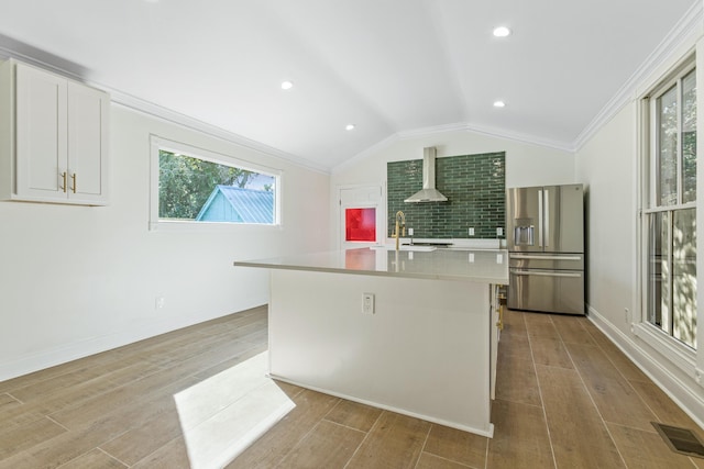 kitchen with stainless steel refrigerator with ice dispenser, white cabinetry, a healthy amount of sunlight, and an island with sink