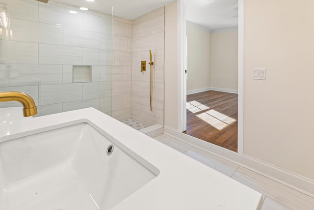 bathroom with hardwood / wood-style flooring, a tile shower, ornamental molding, and sink