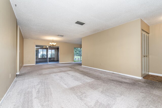 carpeted empty room featuring a chandelier and a textured ceiling