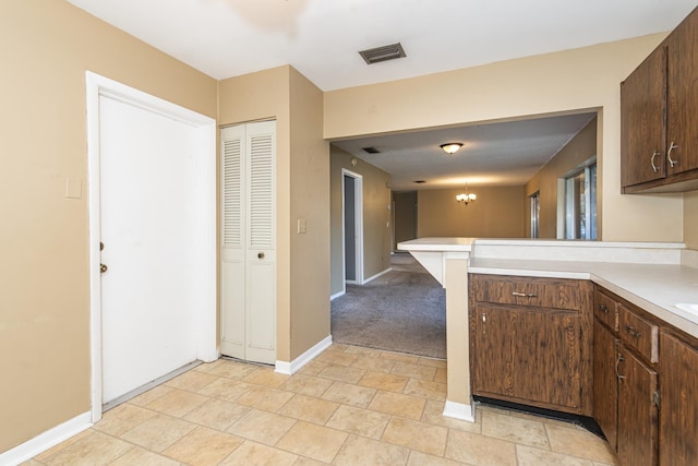 kitchen with kitchen peninsula, light carpet, dark brown cabinets, and a notable chandelier