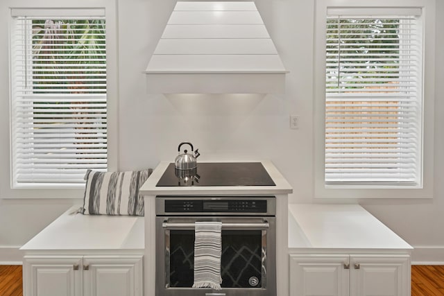 kitchen featuring white cabinets, custom exhaust hood, black electric stovetop, and oven