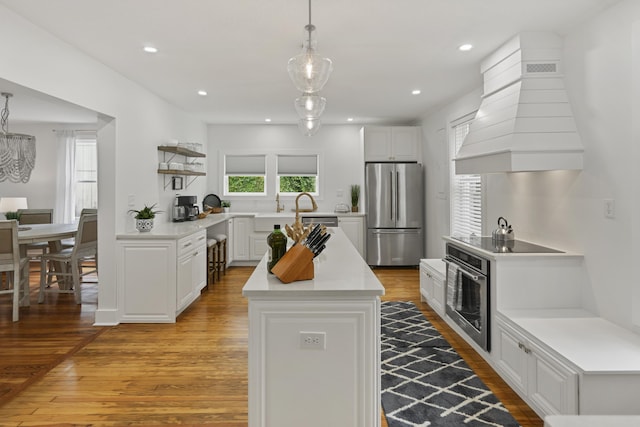 kitchen with appliances with stainless steel finishes, decorative light fixtures, white cabinets, custom exhaust hood, and light hardwood / wood-style flooring