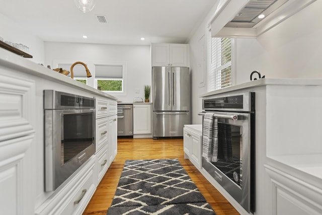 kitchen with white cabinetry, appliances with stainless steel finishes, premium range hood, and plenty of natural light