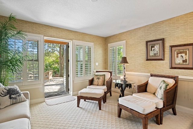 living area with wallpapered walls, a wainscoted wall, light colored carpet, a textured ceiling, and baseboards