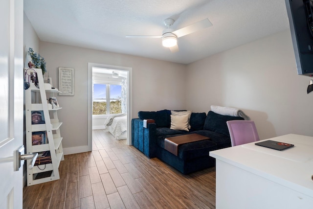 living room with ceiling fan, a textured ceiling, baseboards, and dark wood-style flooring