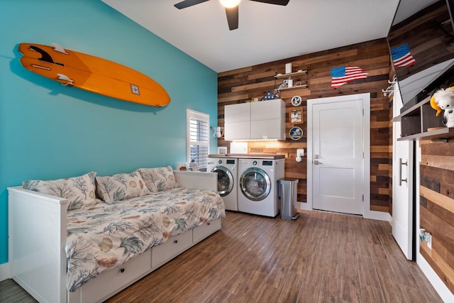 washroom featuring wood walls, wood finished floors, a ceiling fan, cabinet space, and washing machine and clothes dryer