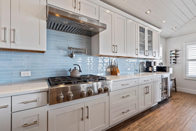 kitchen with lofted ceiling, stainless steel gas cooktop, white cabinets, light countertops, and ventilation hood